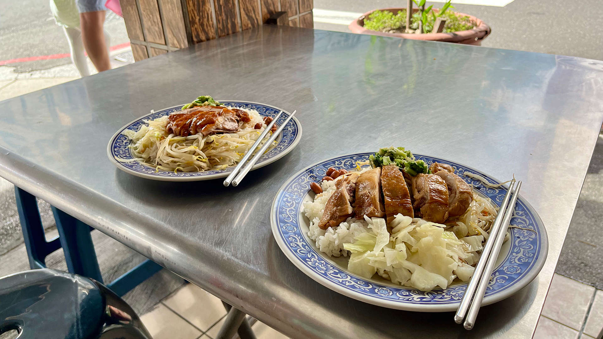 Two lunch dishes on a street-side metal table, with metal chopsticks.