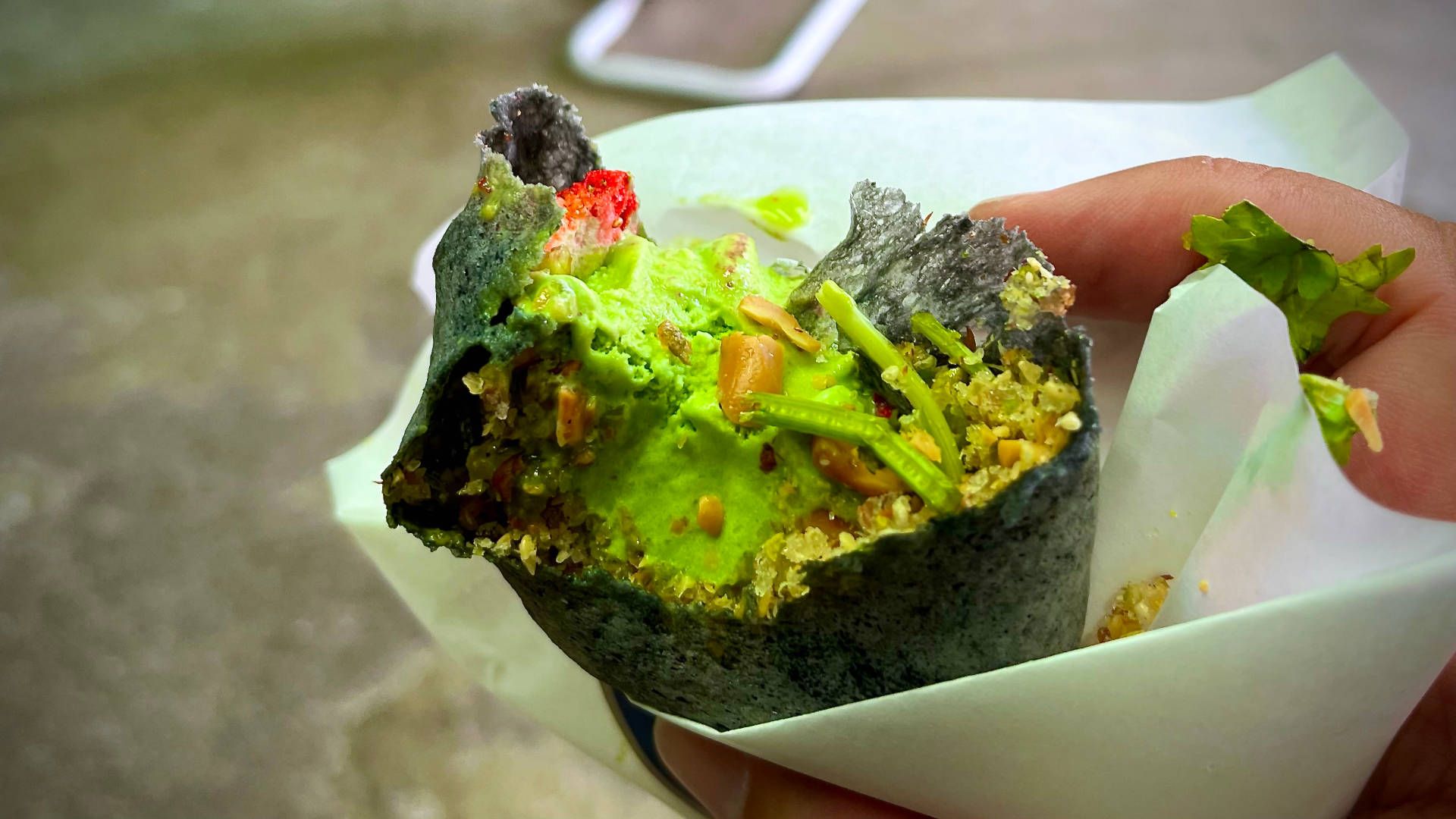 Half-eaten green ice cream with chopped peanuts and cilantro, and frozen strawberries, in a black wrap.