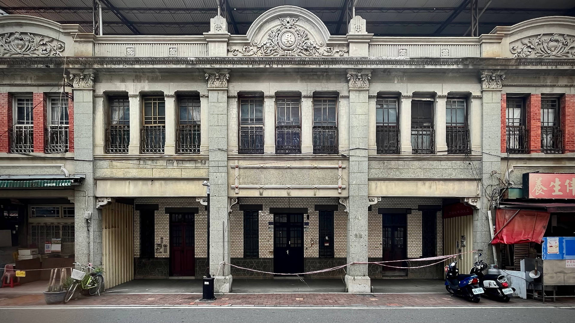 A two-story historic building covered on top by a metal roofing structure, which has been installed approximately three meters above the building’s roof.