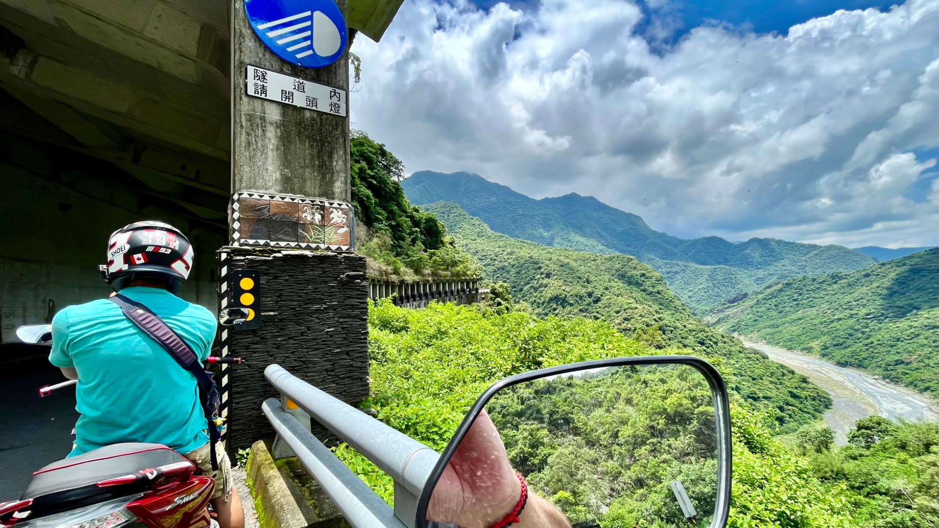 View of a river valley surrounded by forest-clad mountains. The photo is taken at the entrance to a tunnel, which is adorned with ceramic tile art depicting flowers and a clay pot.