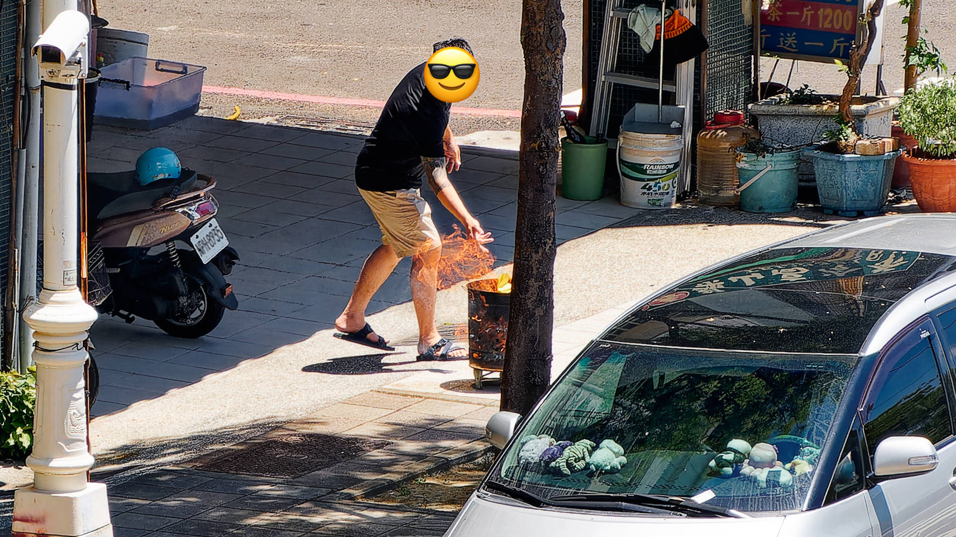 A man tossing yellow paper into a fire inside a metal bucket on the pavement.