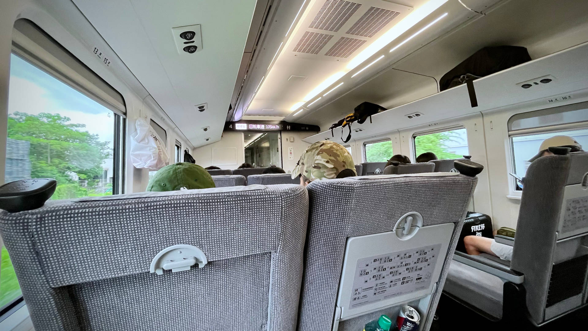Interior of a train carriage. There are two seats each side of the aisle, and lush-looking scenery outside the windows.