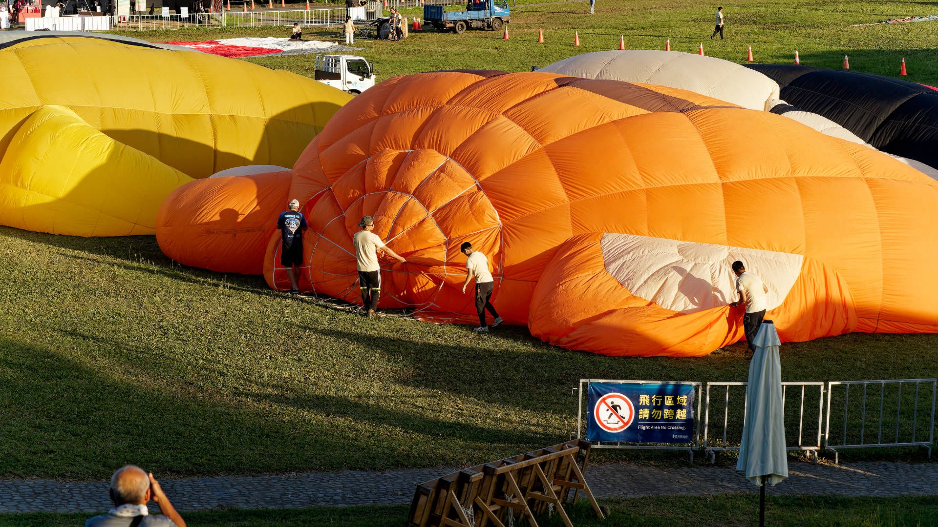 A partially-inflated hot air ballon. Four people are holding various parts of the balloon as it inflates. At this stage, it is still laying across the grass.