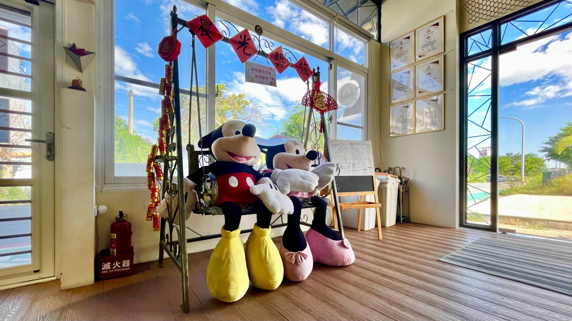 Large Mickey Mouse and Minnie Mouse soft toys placed on a swinging porch chair, in the lobby of a hotel.