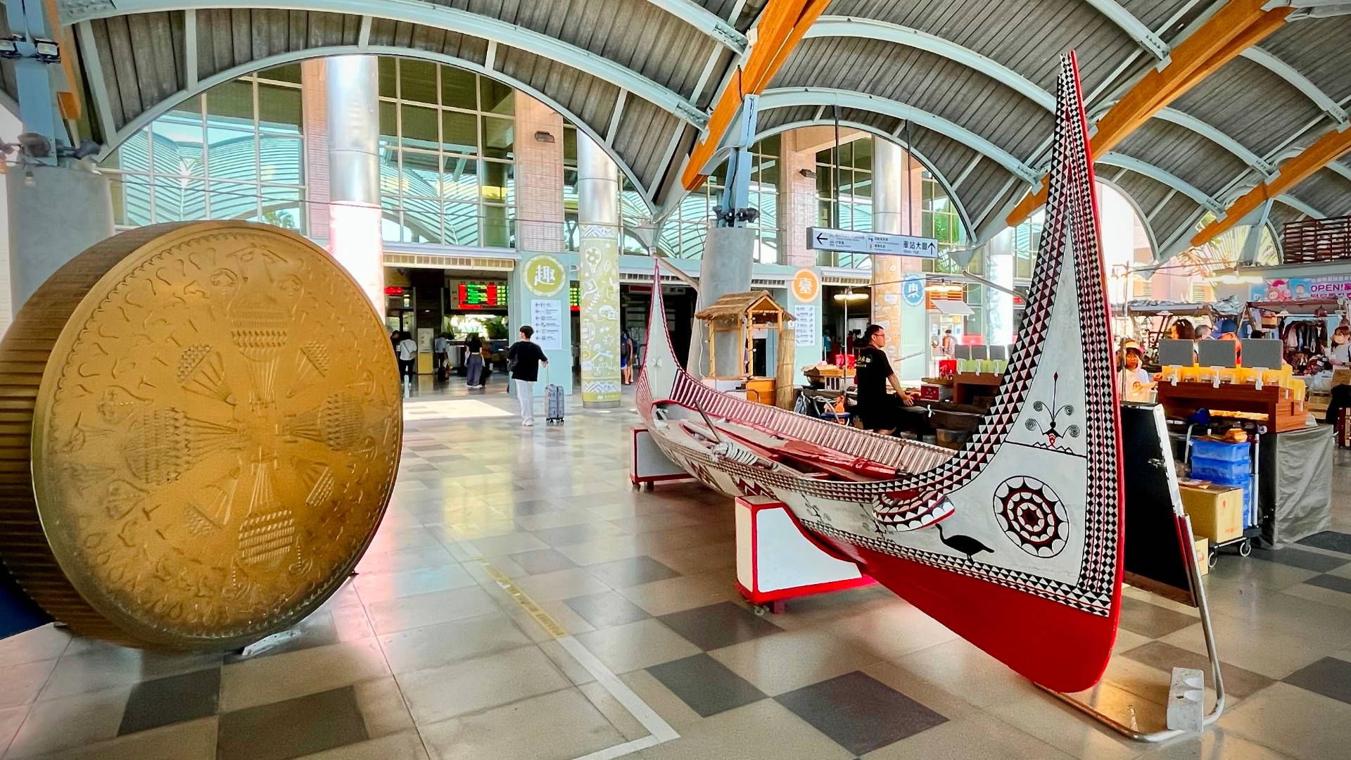 An intricately-painted indigenous canoe on a display stand under the roof of the station. The canoe is approximately 10 meters long with sharply upturned ends that stretch a meter in to the sky. It looks like it may accommodate 2–4 paddlers.