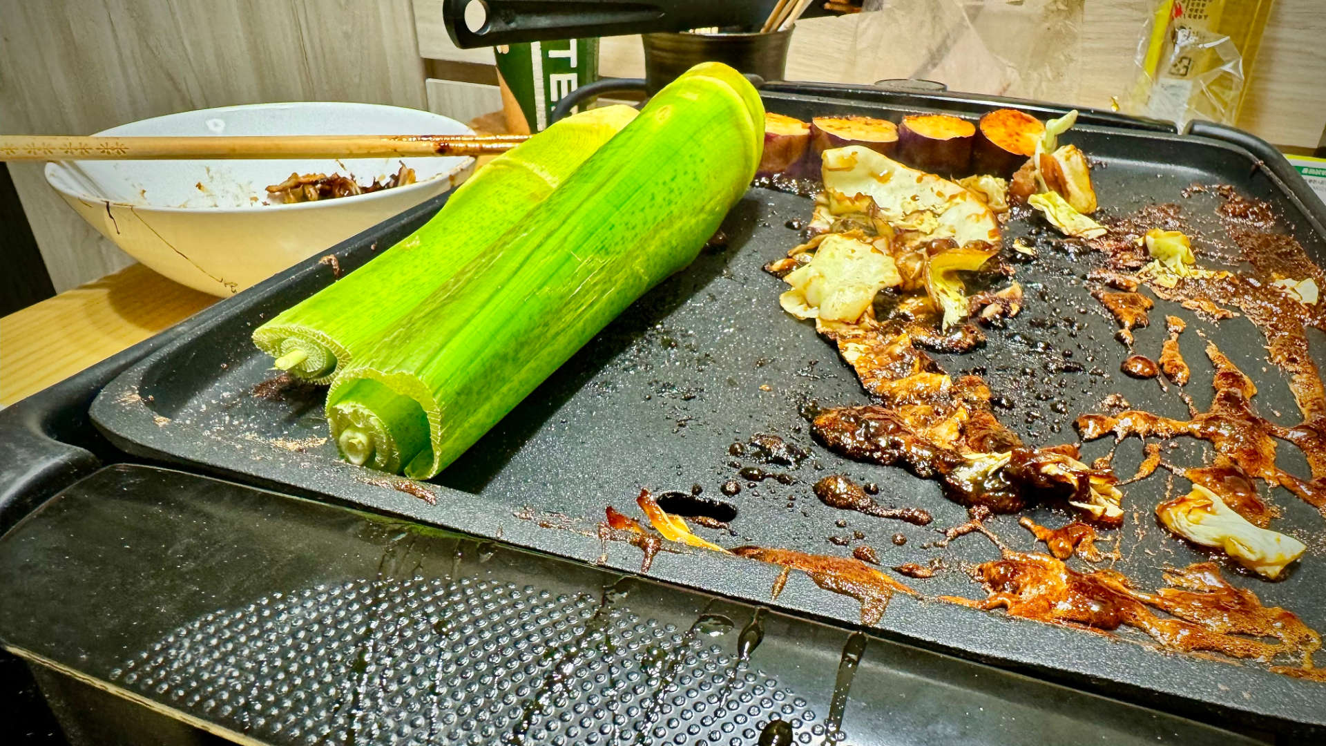 Bamboo, cabbage, and eggplant being cooked on an indoor electric barbeque.