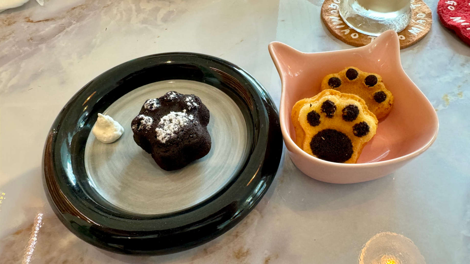 A plate plate with a cat-paw-shaped brownie, and a cat-shaped bowl containing two cat-paw-shaped cookies.