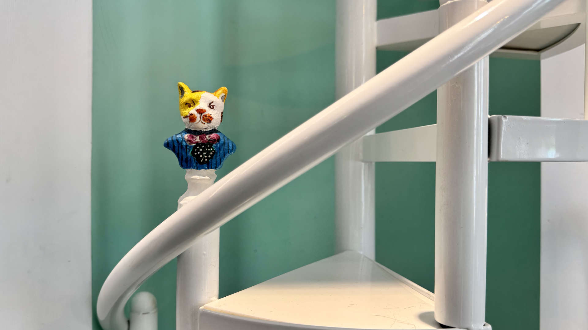 A cat-sized spiral stair case, with a small cat-in-formal-attire model affixed to one side.