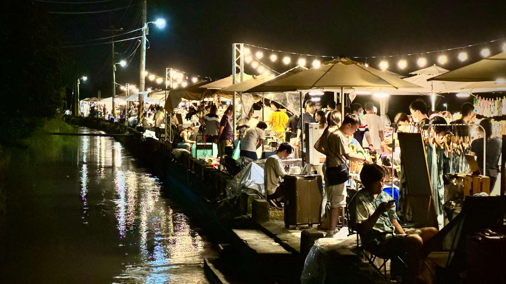 Market stalls, crowded with people, alongside a canal.