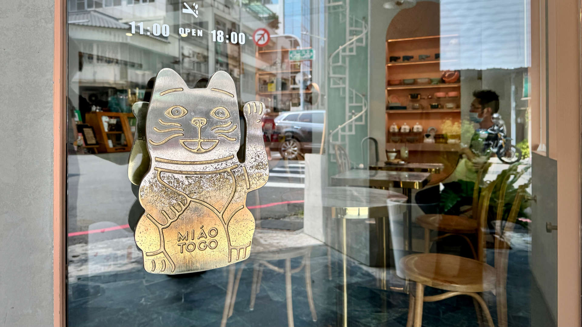 A large brass door handle on a glass door. The handle is in the shape of a beckoning cat.