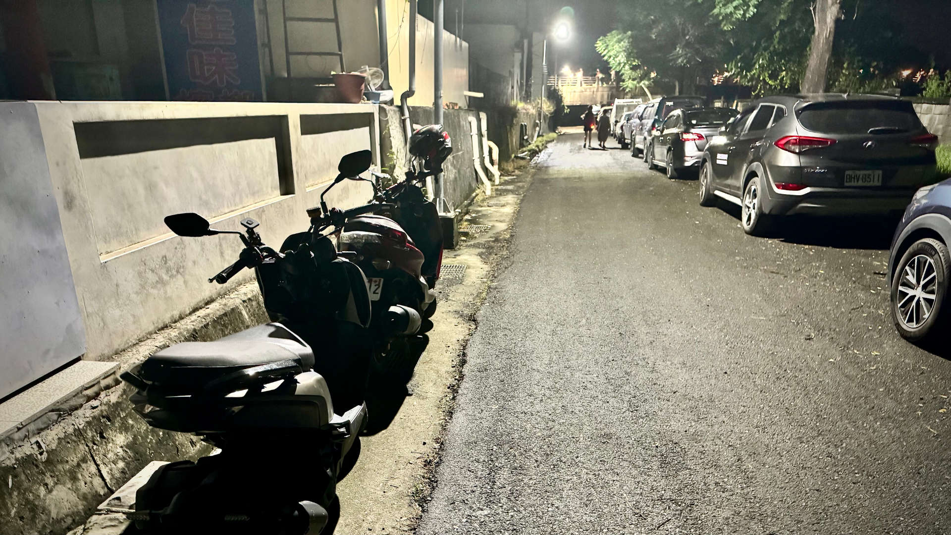 Scooters and cars parked in an alleyway at night.