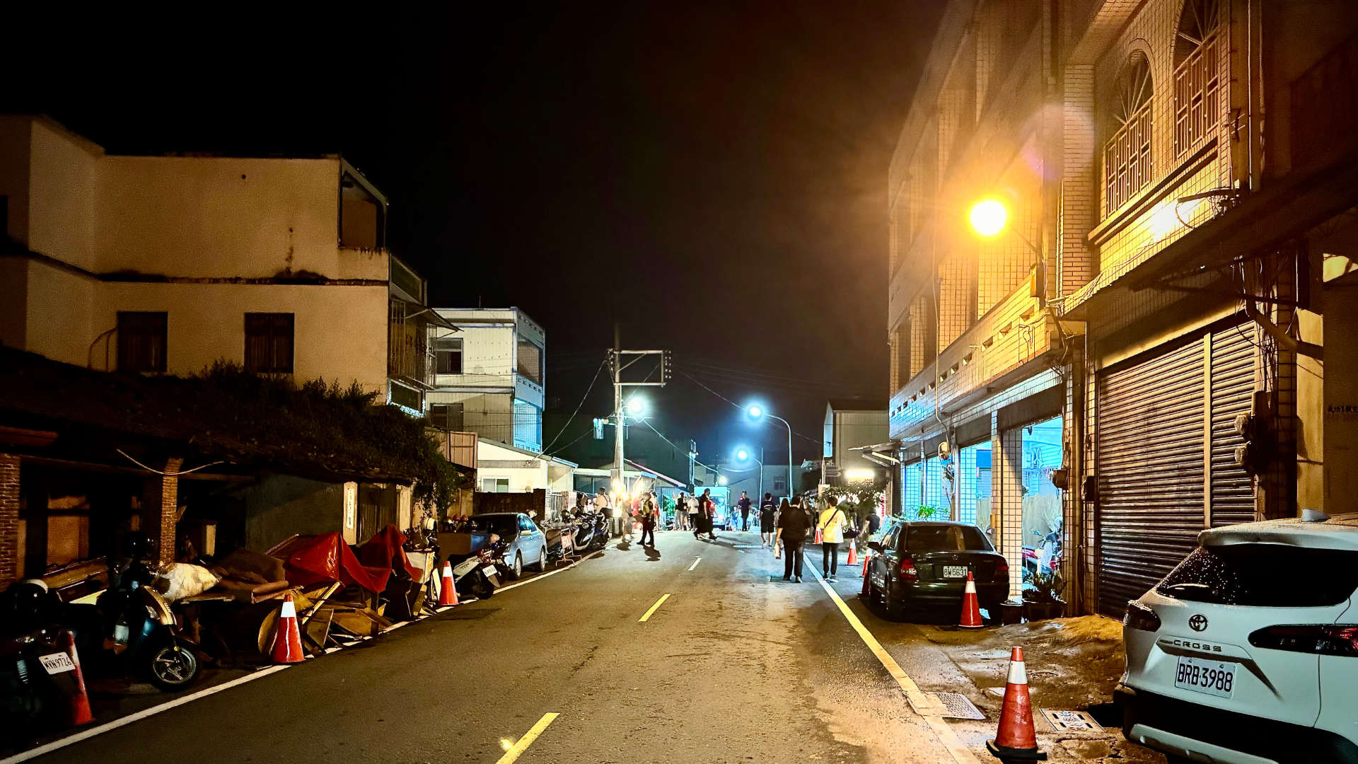 An empty street in Meikong, Taiwan, at night. There are crowds of people in the distance.