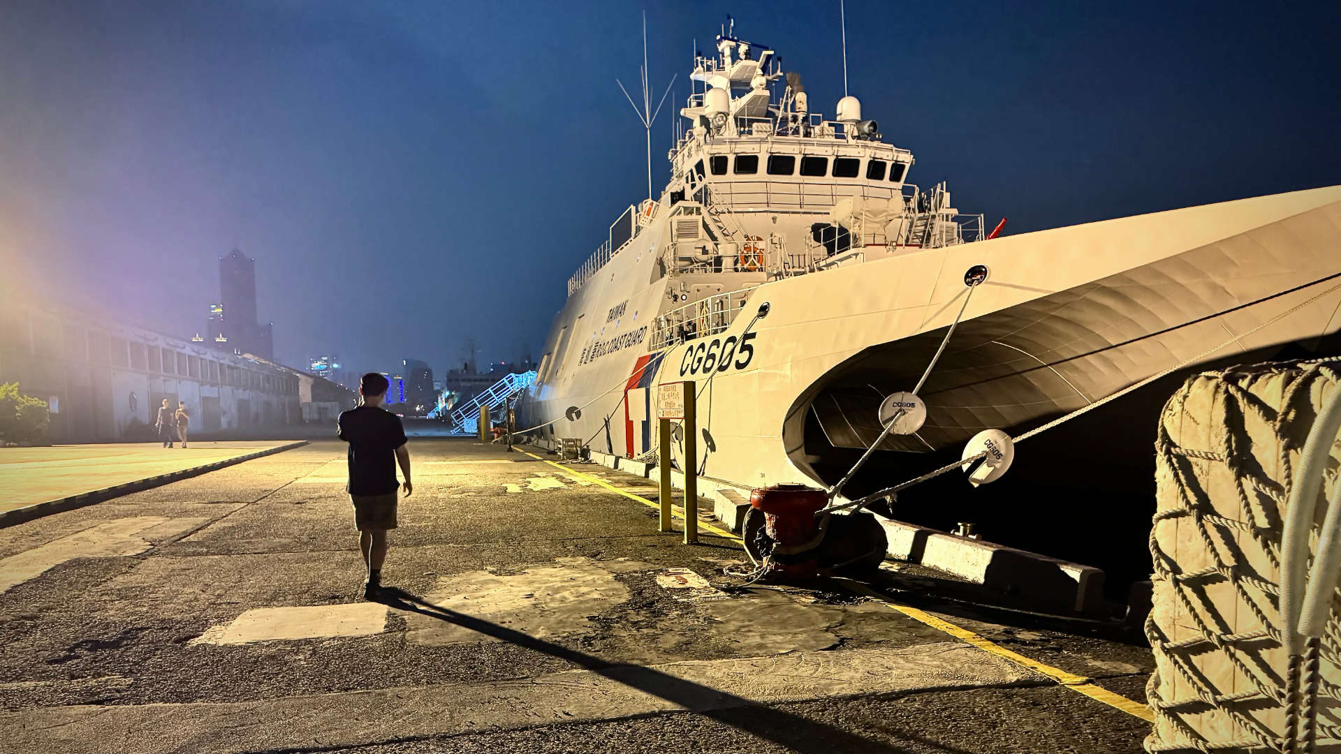 Silhouette of a man walking past a Taiwan Coast Guard offshore patrol catamaran docked at Kaohsiung Harbor at night.