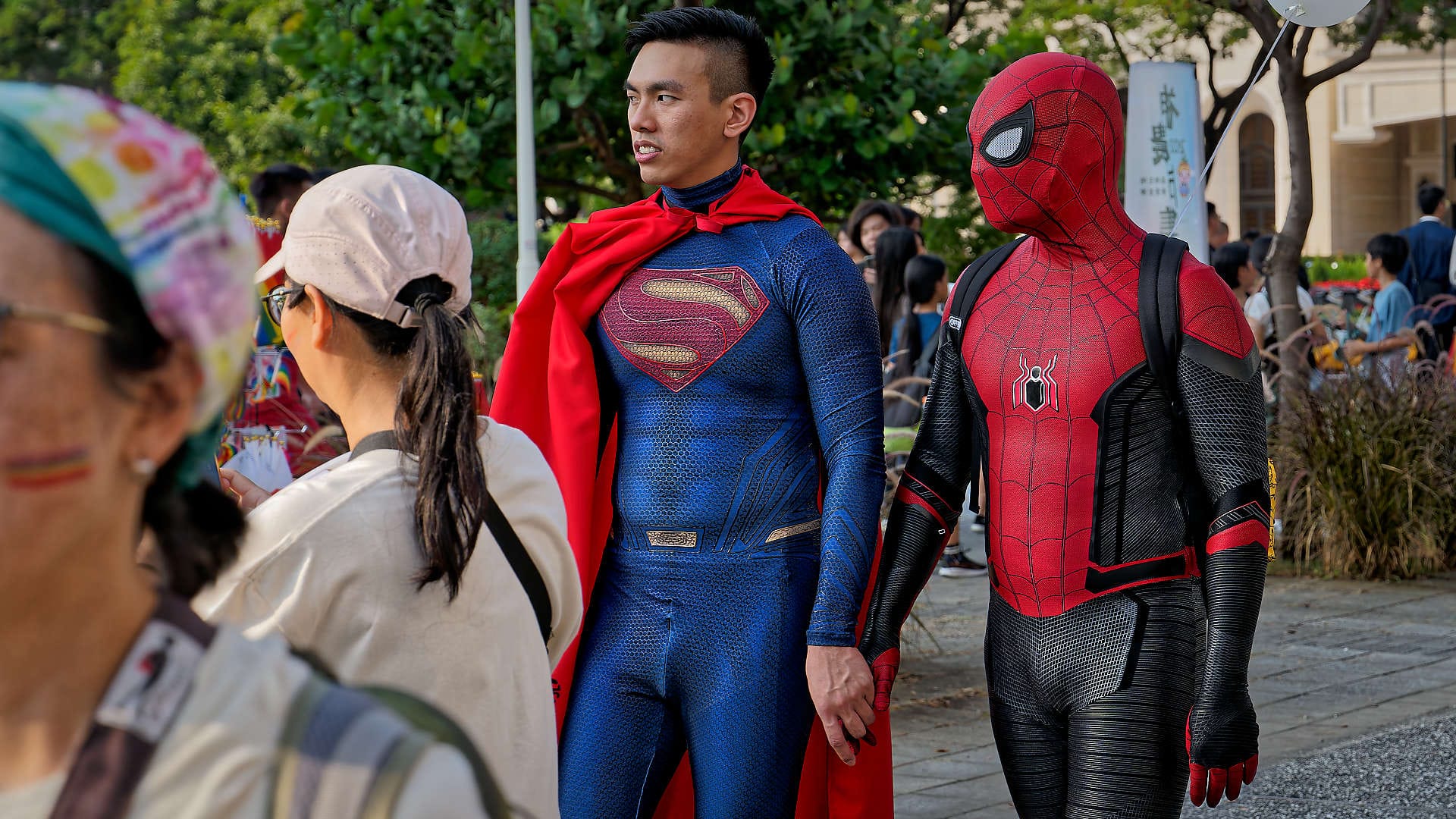 Person dressed as Superman holding hands with person dressed as Spiderman.