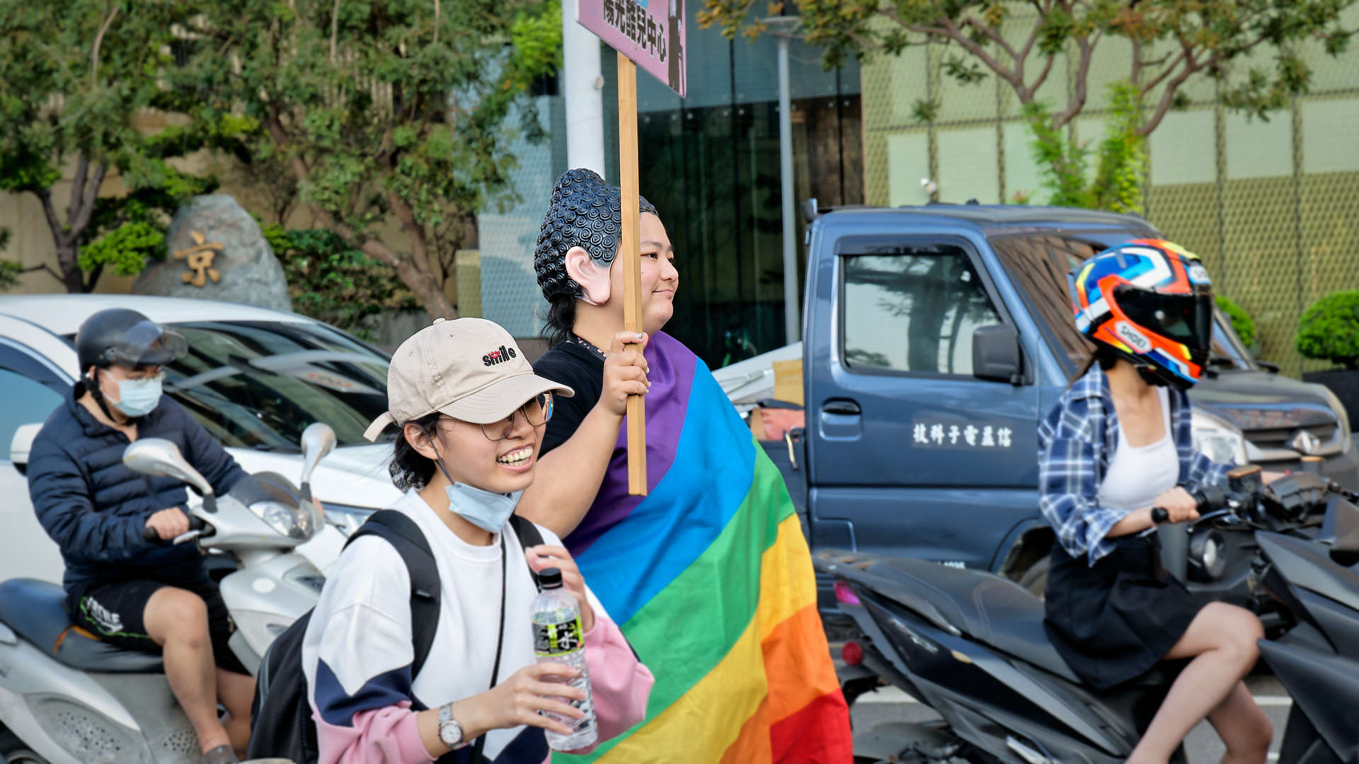 Person in costume and wrapped in a rainbow flag.