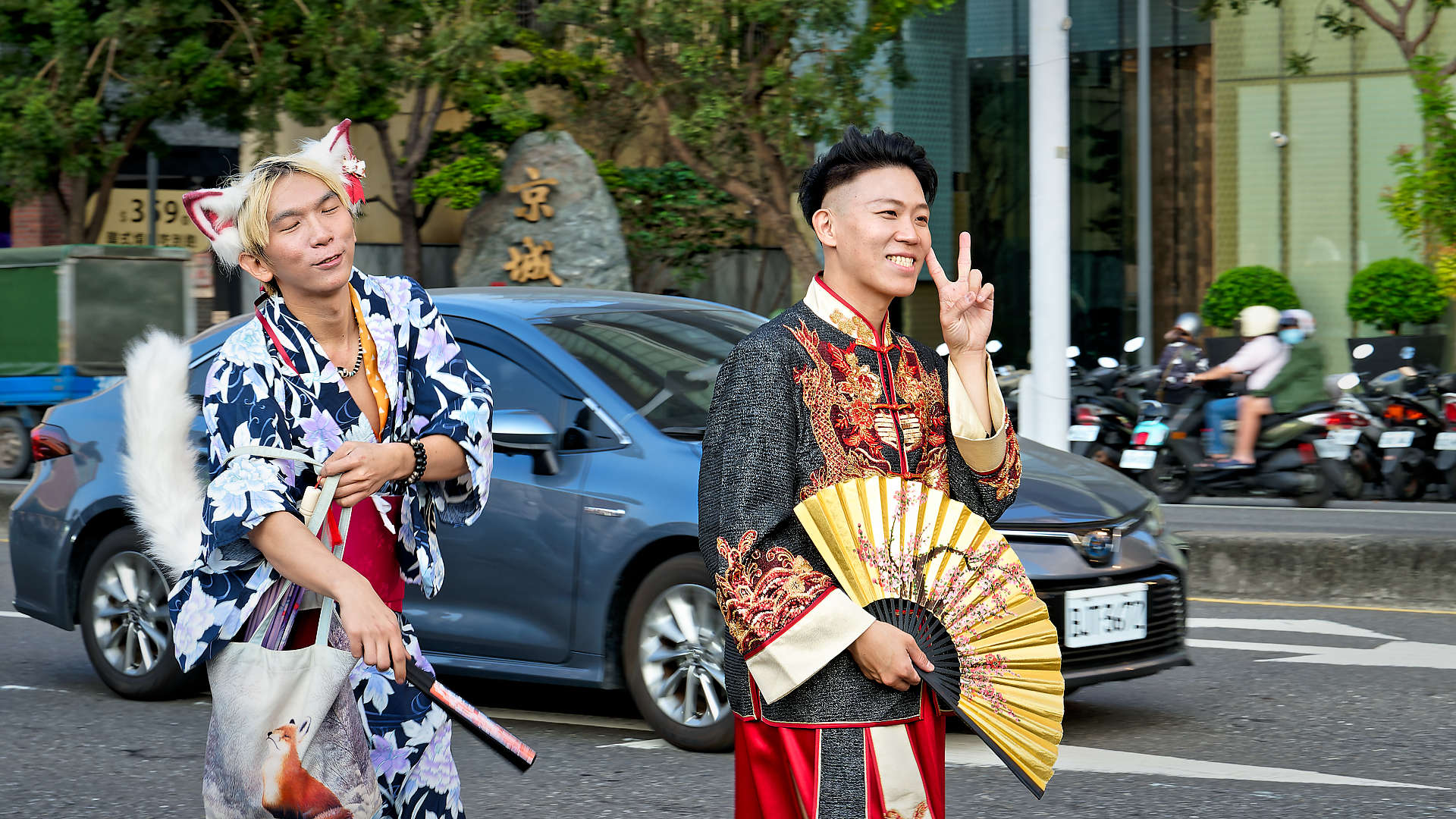 Two men in costume, walking in the Kaohsiung Pride parade. One is giving a peace sign with his left hand.