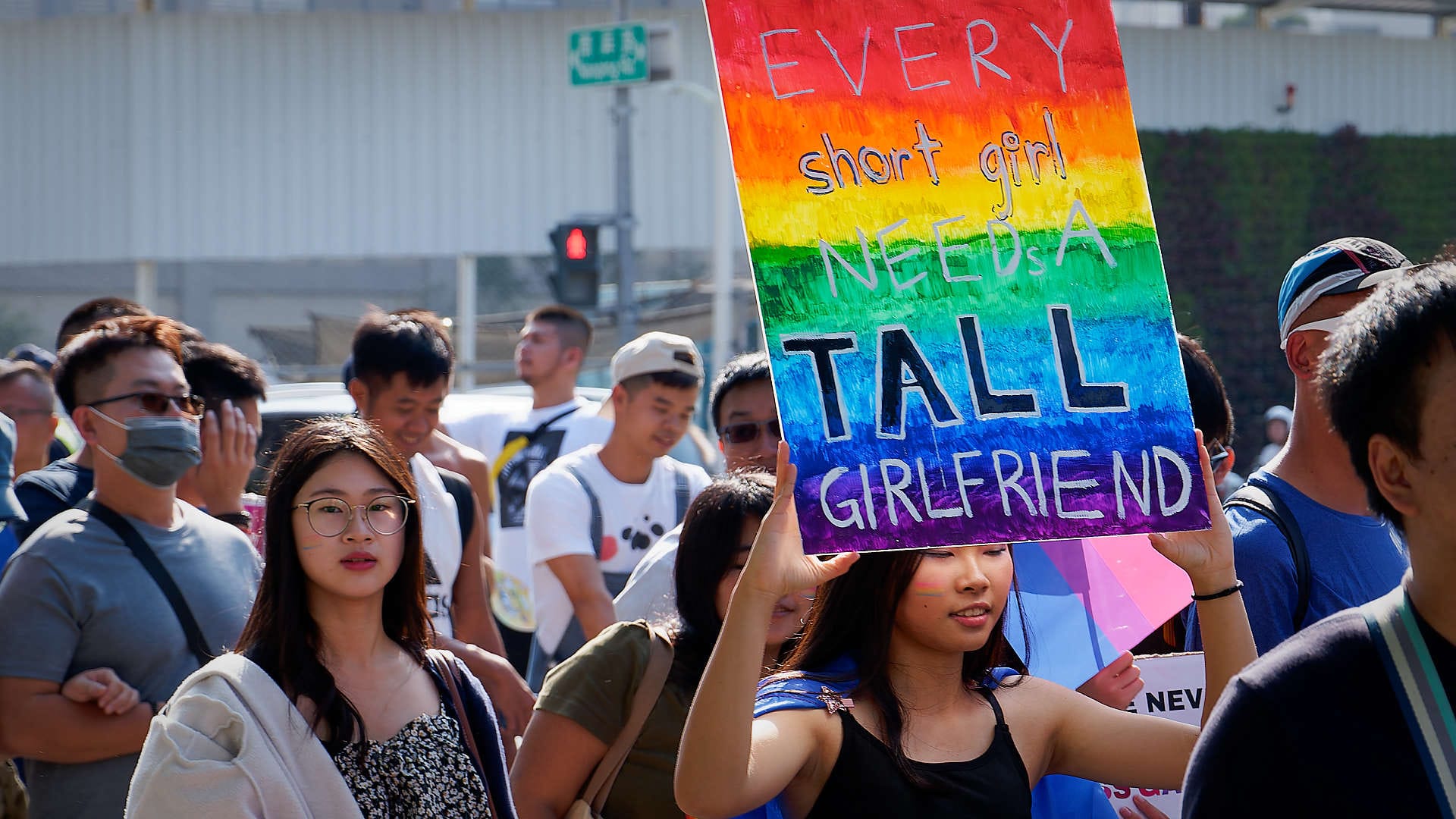 Woman in the Kaohsiung Pride Parade holding a colorful sign that says “Every short girl needs a tall girlfriend”.