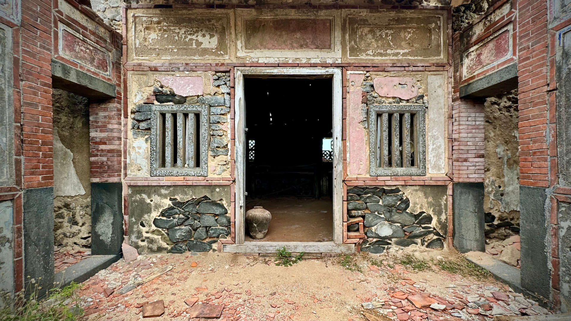 Inner courtyard of an abandoned stone and brick house, with a large clay container in a doorway.