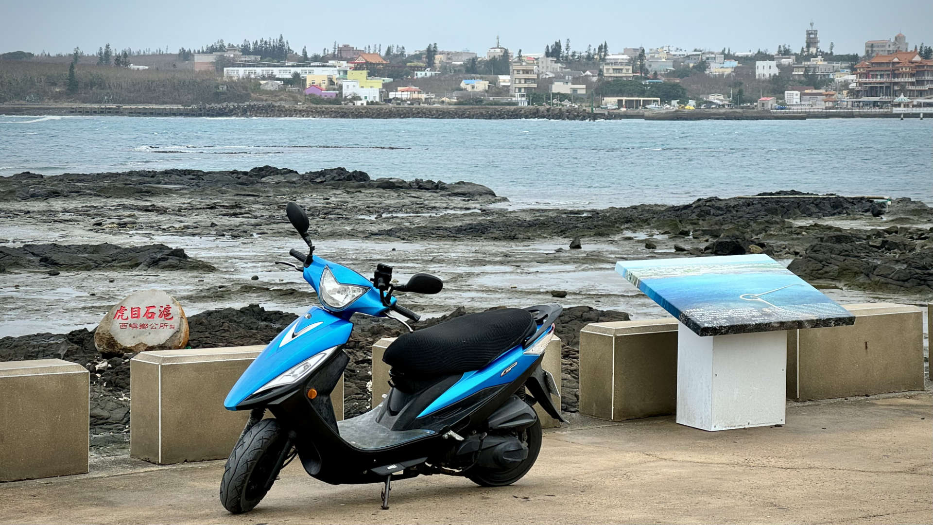 A scooter parked near a rocky foreshore.