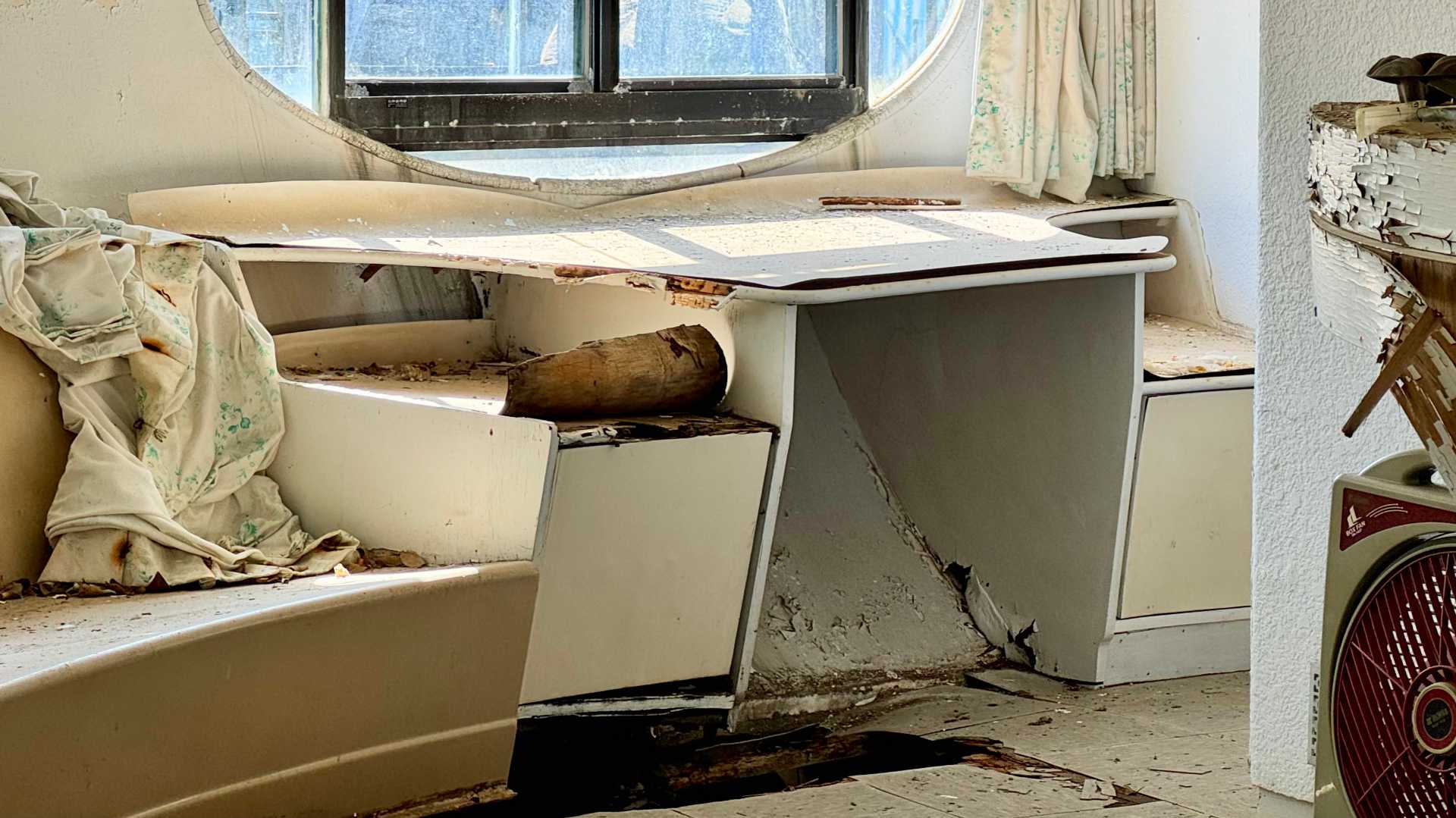 Rotting inbuilt furniture above a hole in the floor. Soft coverings are missing.