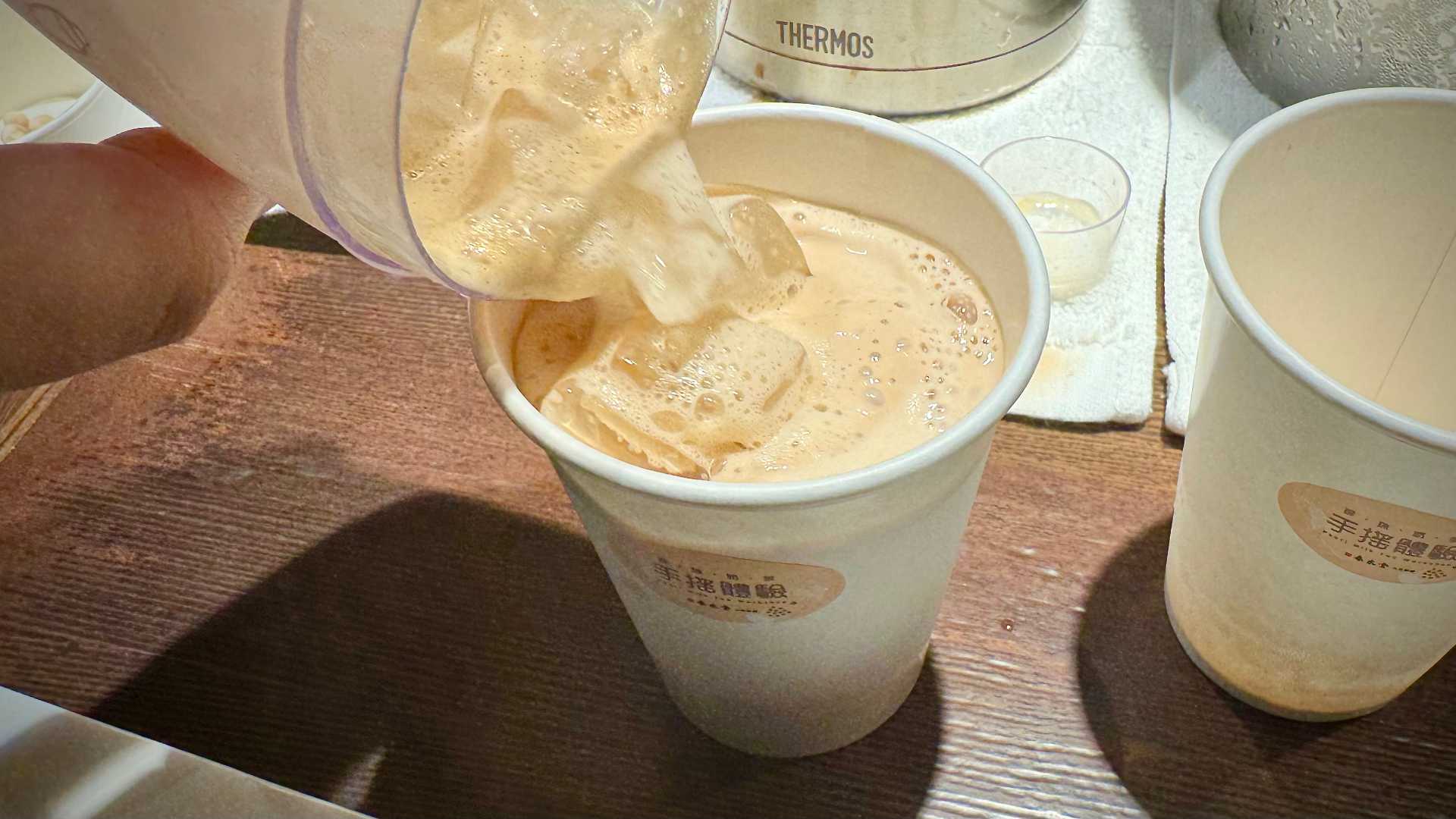 Pouring ice into a paper cup of bubble tea.