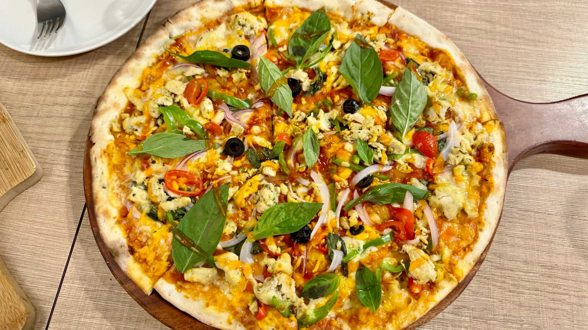 A 12-inch pizza on a thin base, rich in toppings such as basil leaves, onion, tomato, peppers, capsicum, chillies, corn, and chicken.