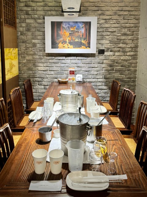 Eight chairs around a long wooden table. The tabletop is covered in disposable cups, ice buckets, and various ingredients and tools.