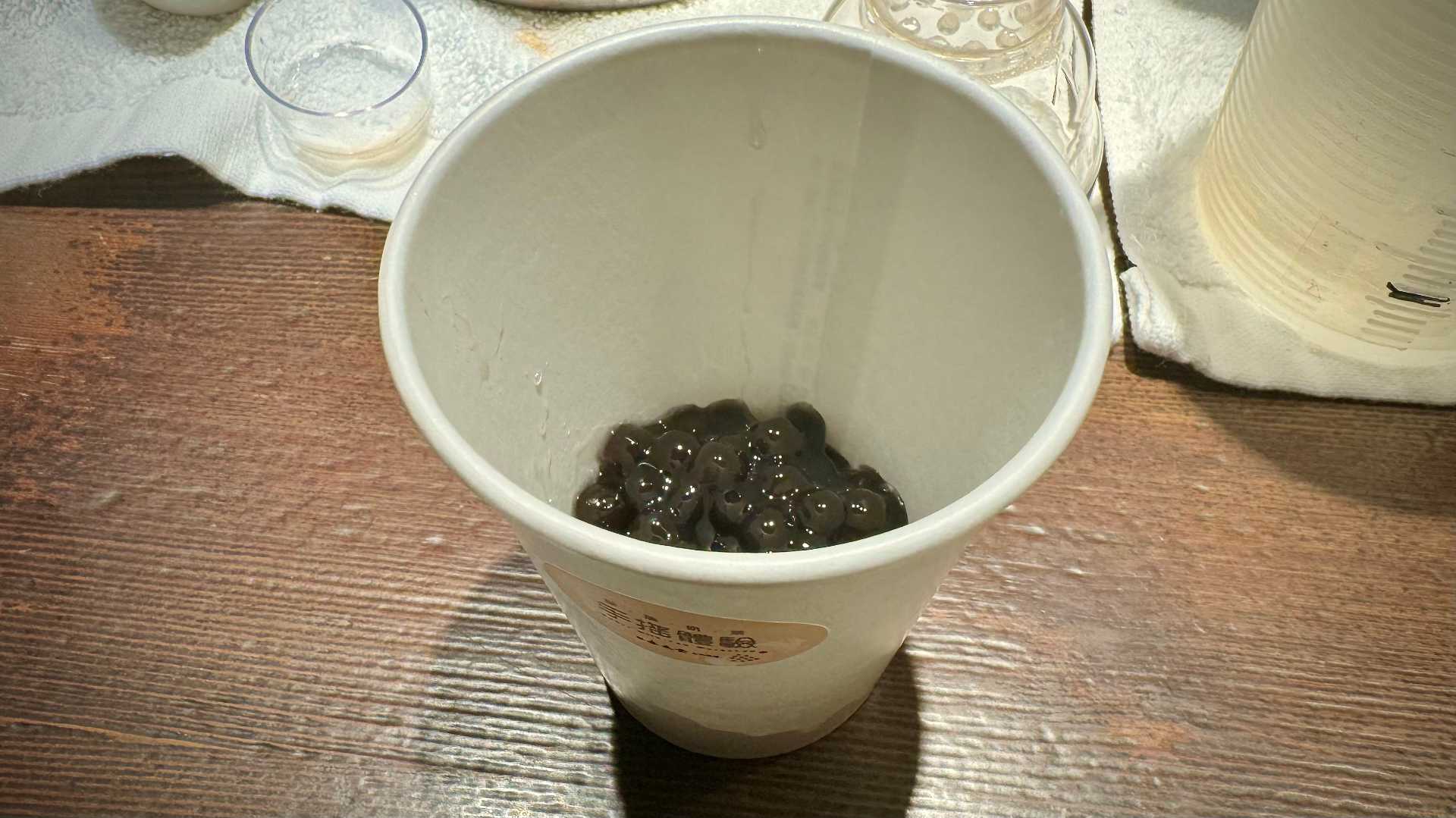 A few dozen cooked black tapioca balls in a paper cup.