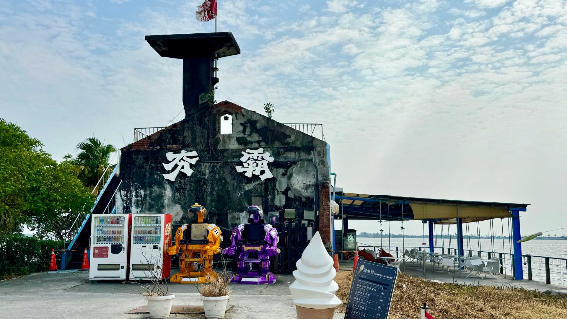 A historic concrete-and-brick seaplane traffic control tower. Vending machines and human-sized robot figures stand outside.