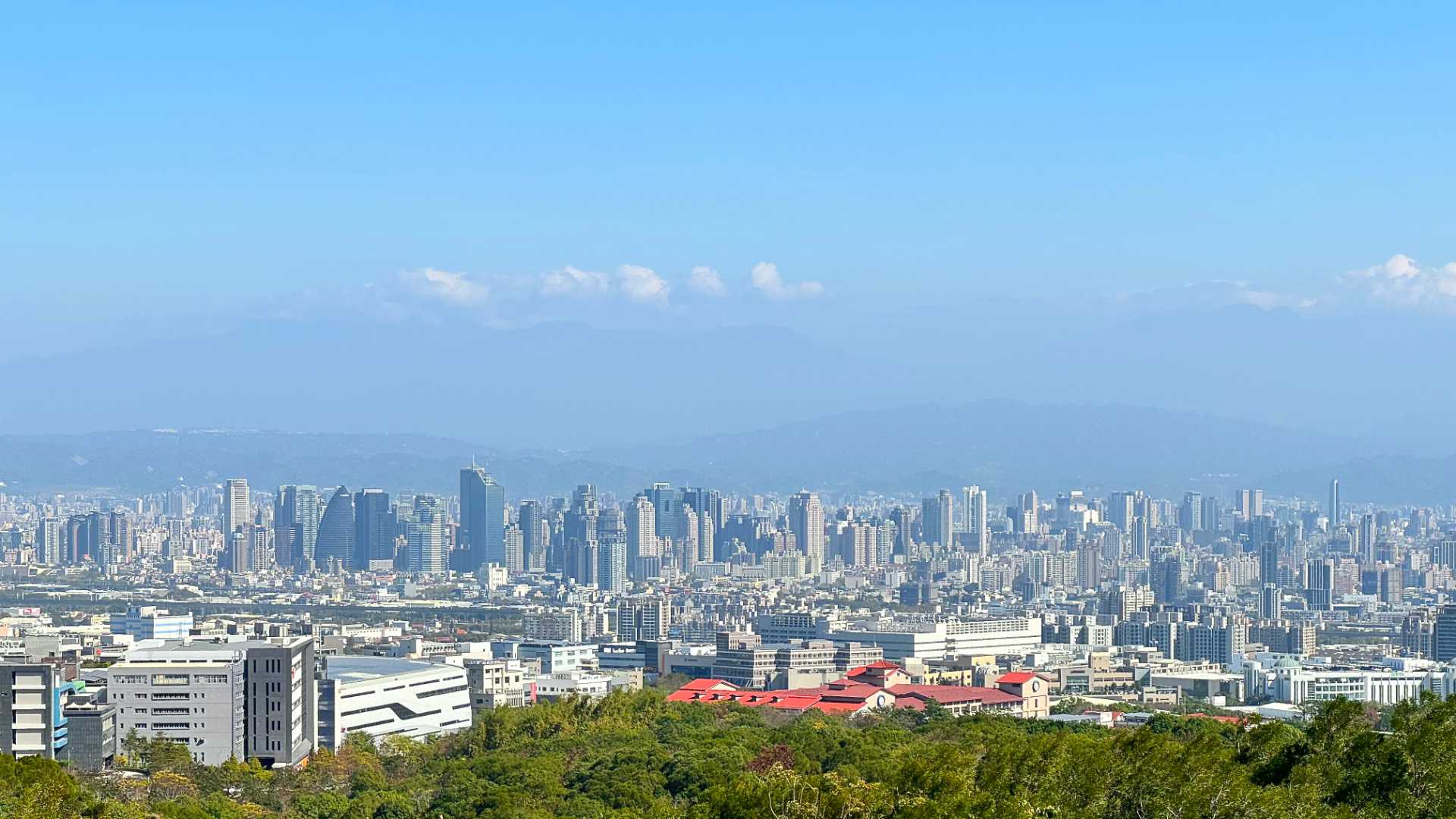A wide-angle photo of the Taichung City skyline. It’s a beautiful sunny day. The skyline comprizes dozens (or hundreds) of high-rise buildings.