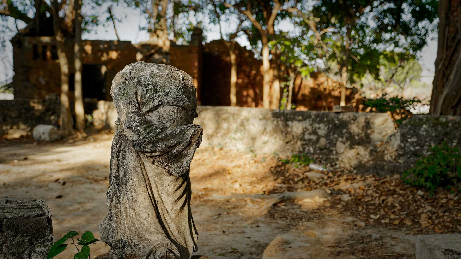 A deteriorating stone statue of a woman draped in a long dress, without a head, on the grounds of Minxiong Haunted House. A brick ruin is out of focus in the background.