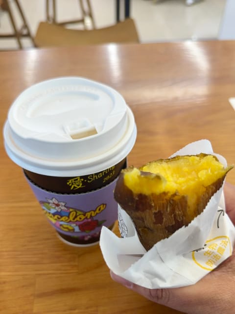 A take-out coffee and a hand holding a paper bag containing a partially-eaten sweet potato.