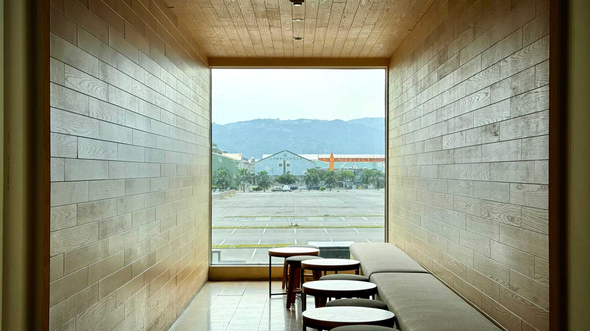 A large window looks out over a carpark at the end of one of the shipping containers. A bench seat and small round tables line the right wall.