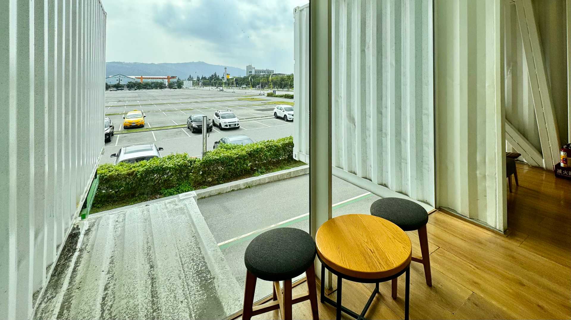 A small round wooden table and two cushioned stools next to a floor-to-ceiling window.