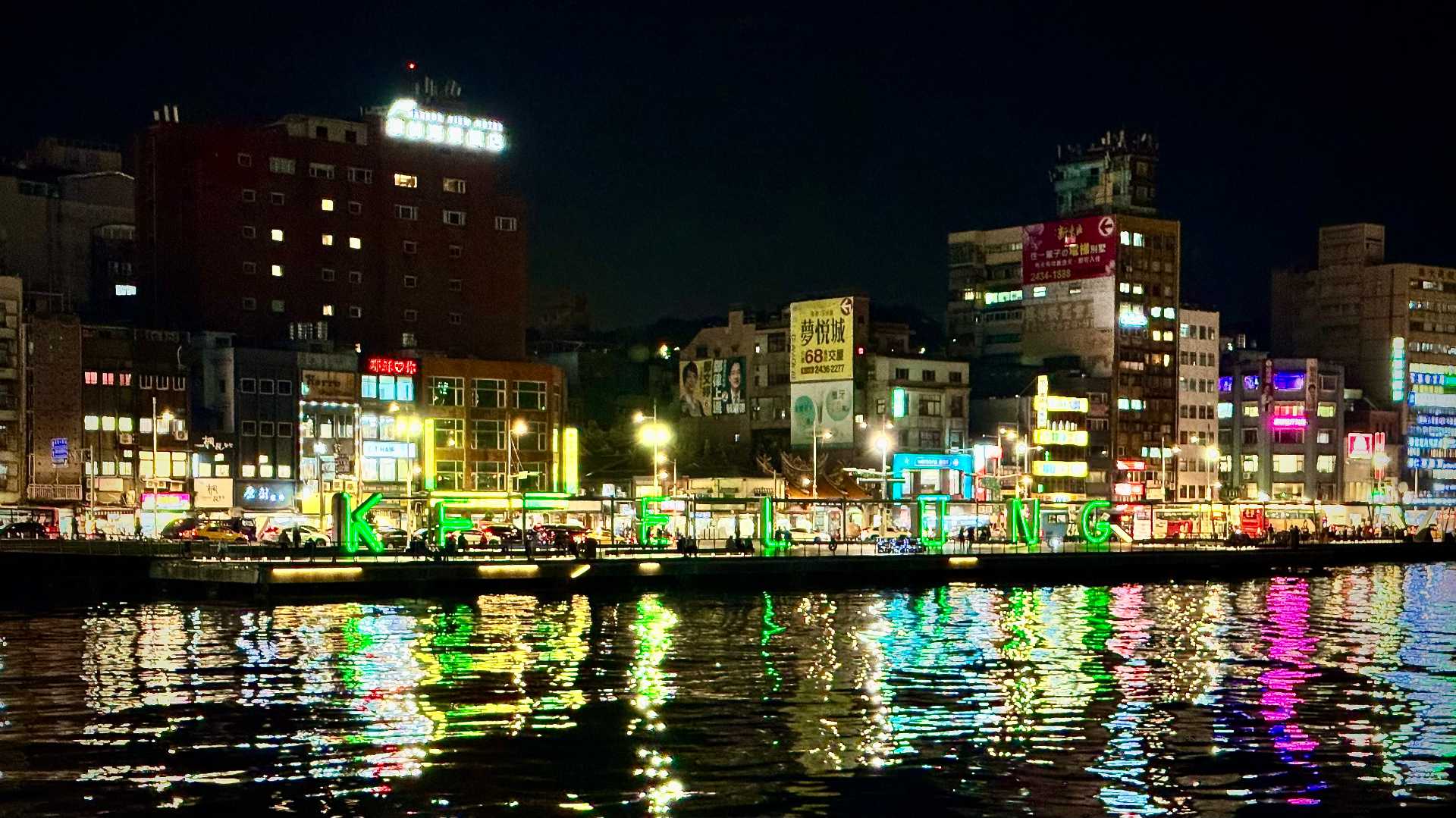 Night-time view of lights reflecting in Keelung Harbor. The letters K-E-E-L-U-N-G, each approximately one-story-tall, are illuminated on the far side of the harbor.