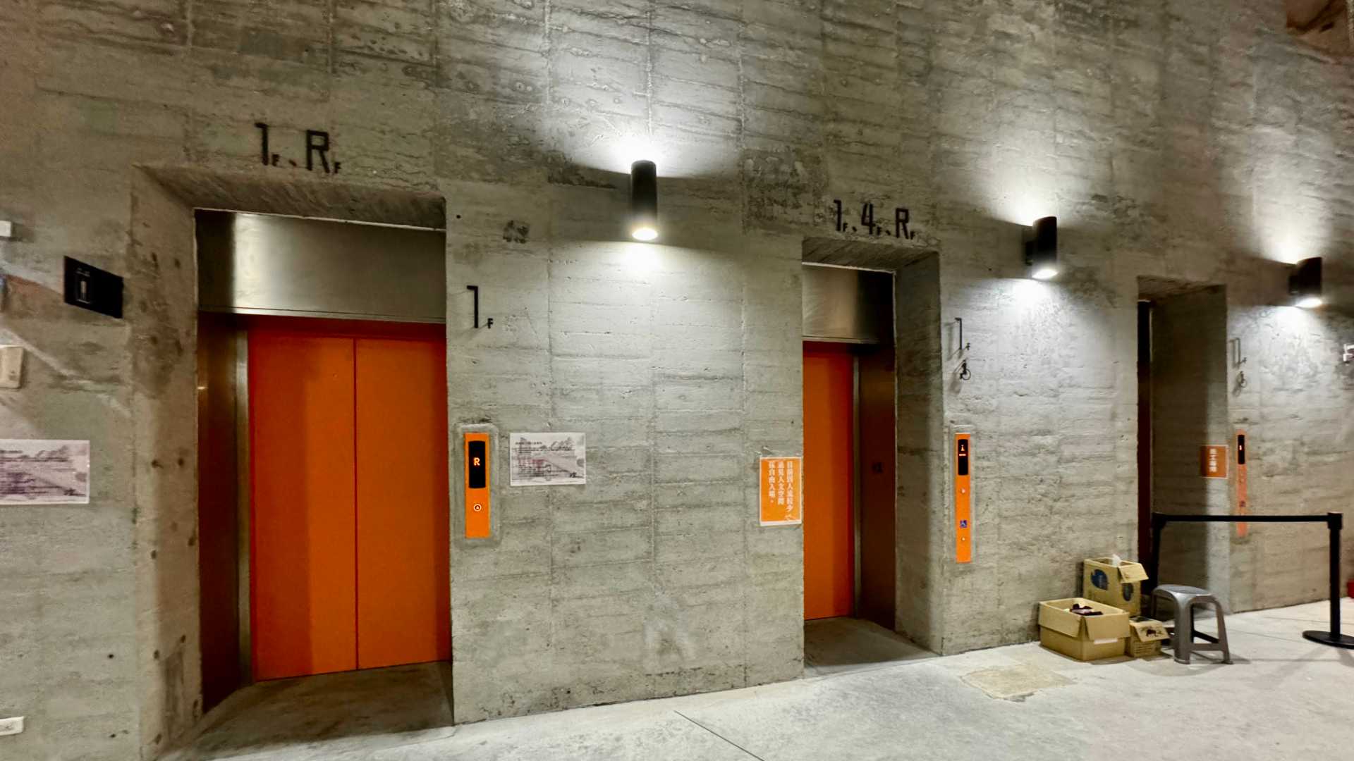 Two elevators inset in an industrial-style concrete wall. The left elevator only stops at the first floor and the roof. The right elevator also stops at the fourth floor.