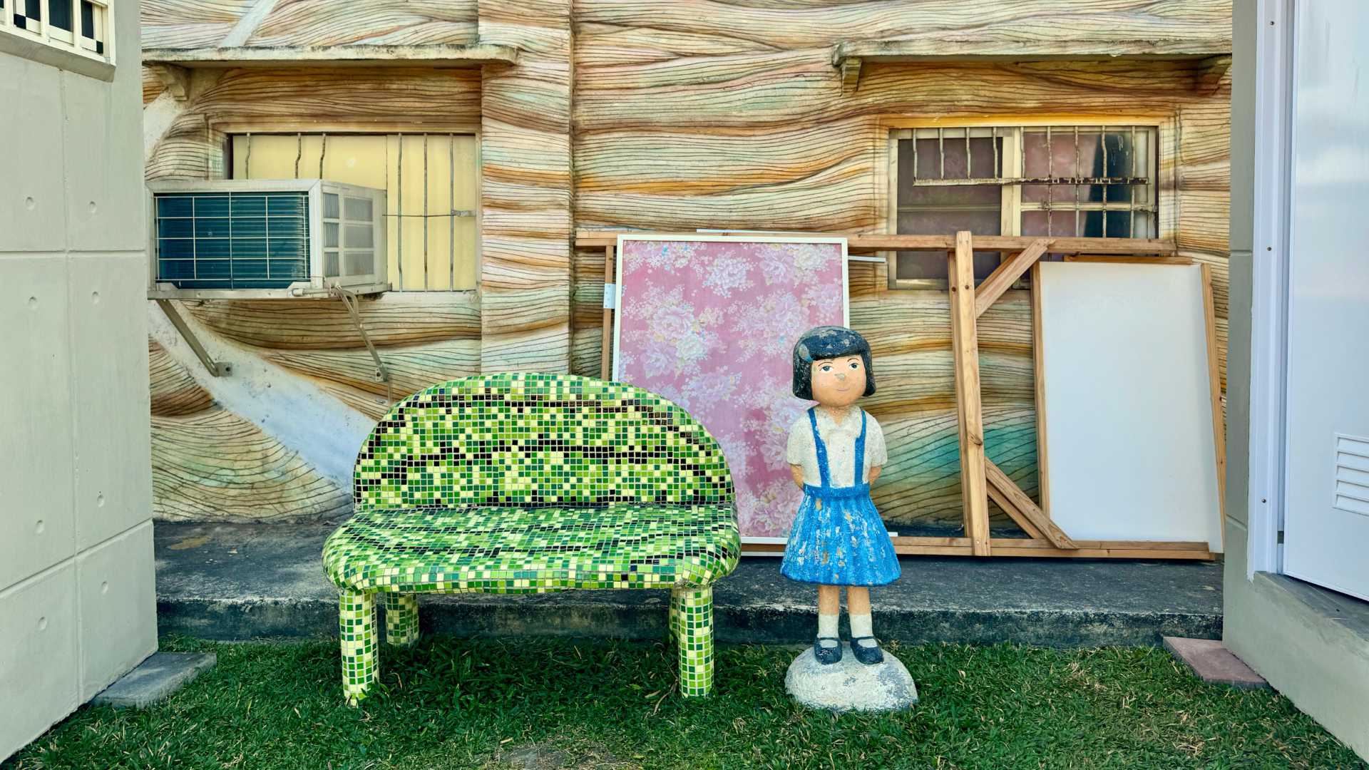 A two-person mosaic chair in the shade between two portable toilets made of concrete.