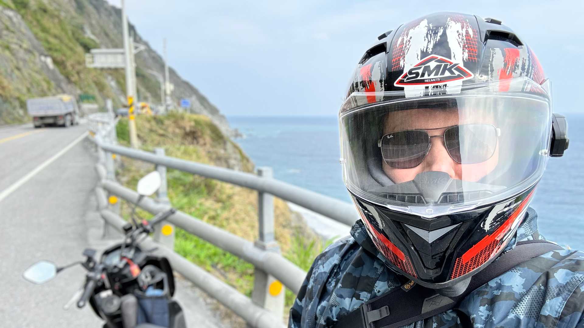 A selfie of the author, Zhen-Kang, in front of a motorcycle, on a two-lane mountain road overlooking the Philippine Sea. Zhen-Kang is wearing sunglasses and a motorcycle helmet.