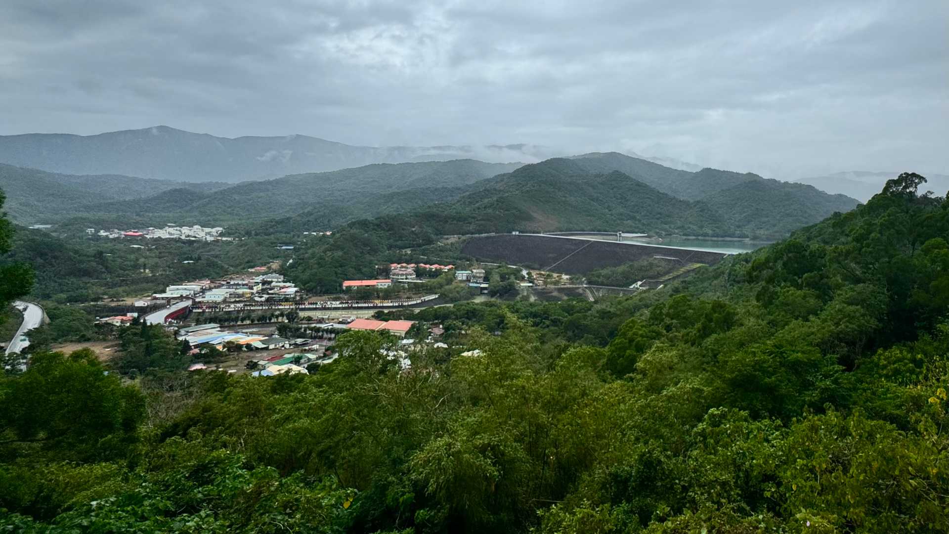 Wide-angle view of Mudan Township beneath a large dam filled with water, and surrounded by bush-clad mountains.