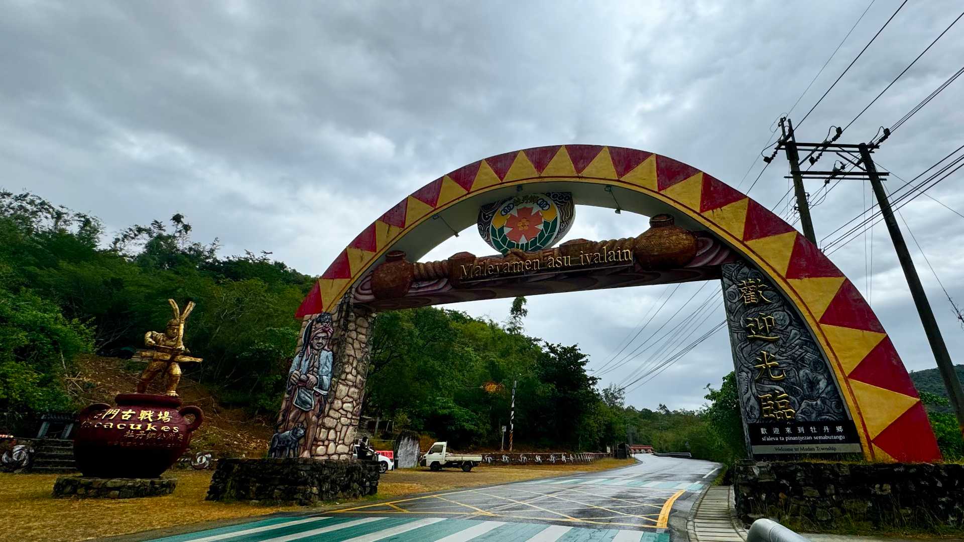 A painted concrete arch over the road marking the entrance to Mudan Township. Welcome is written in Paiwan, Chinese, and English.