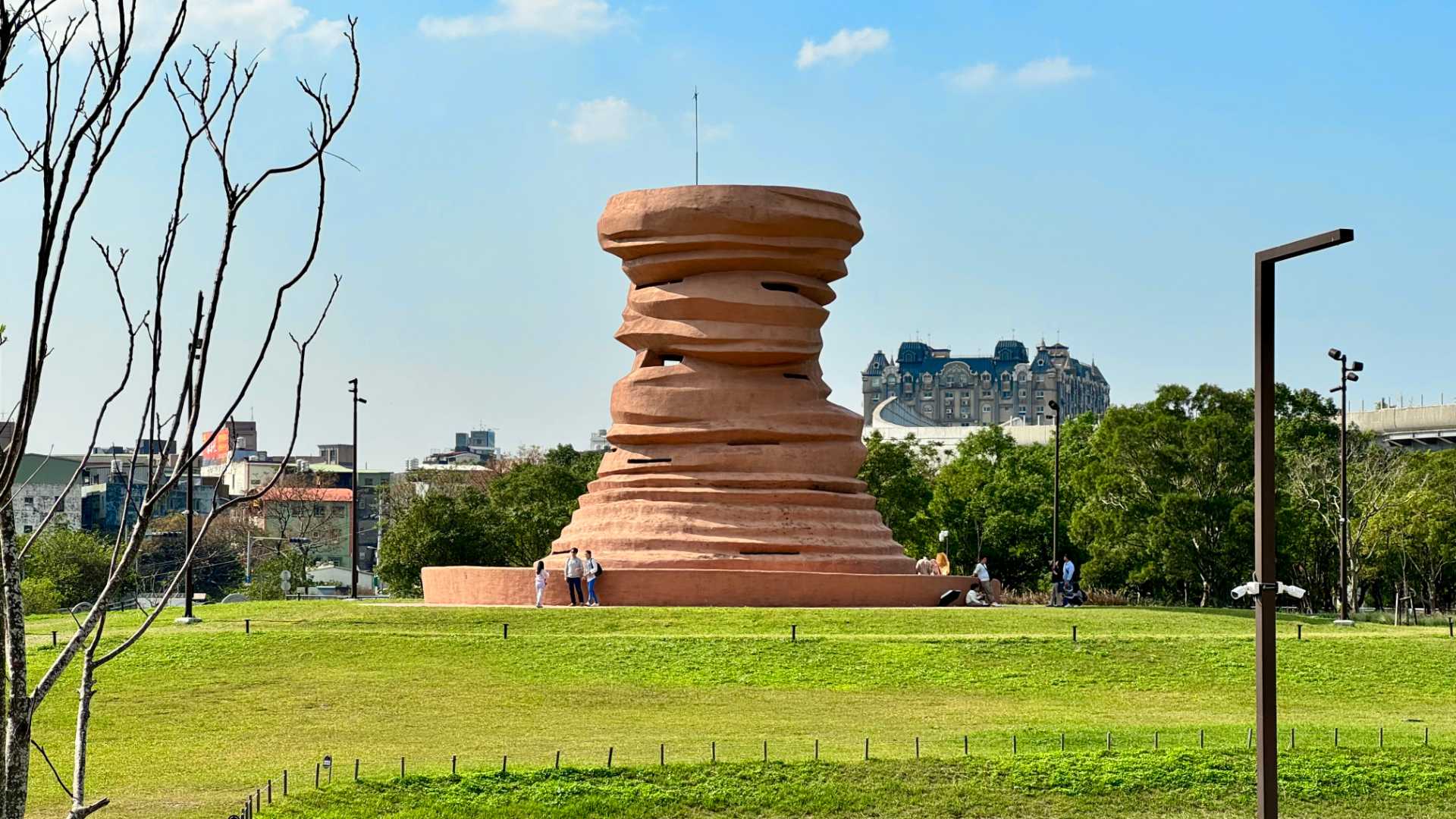 A large ceramic art installation, approximately five stories tall, in the middle of a grassy field. The installation looks like an unrefined clay vase.