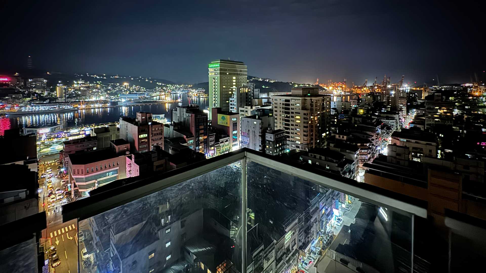 Panoramic view of Keelung City at night. A glass balustrade is visible in the foreground.