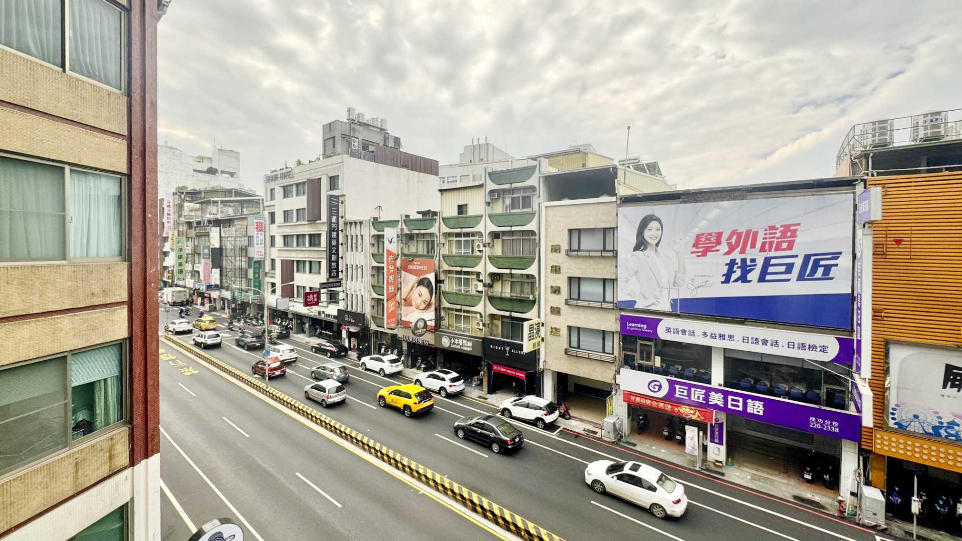 View of a six-lane city street in Tainan, Taiwan. It’s an overcast day. There are four-to-seven-story buildings either side of the road.