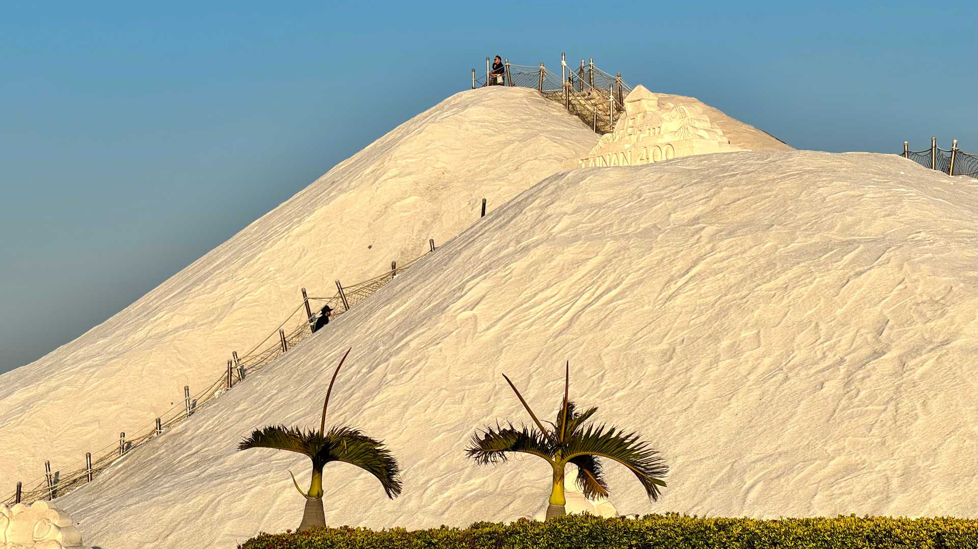 Qigu Salt Mountain just ahead of sunset. The salt mountain is 6 stories tall and has a walkway up two sides. The walkway has guide ropes strung between metal poles. Near the top of the salt mountain is a sculpture that includes the words ‘TAINAN 400’.