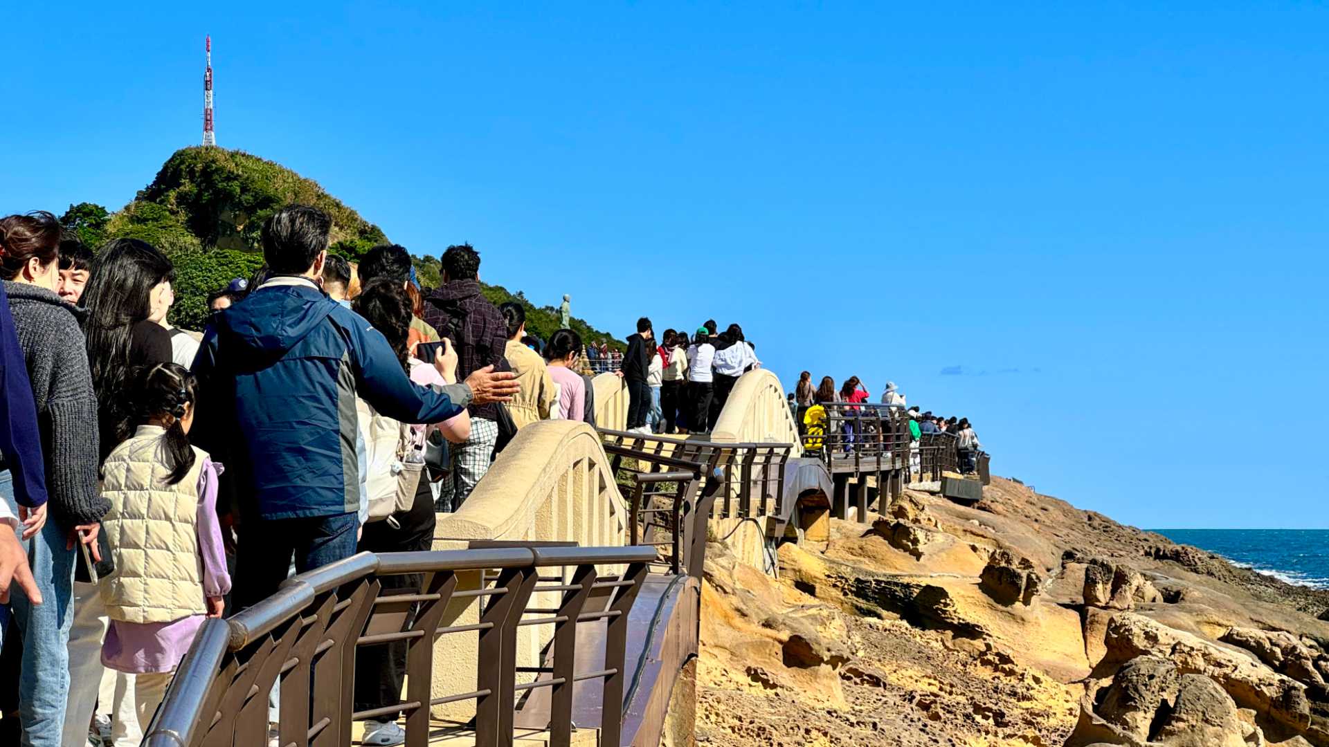 A queue of hundreds of people walking on a pathway next to the shore.