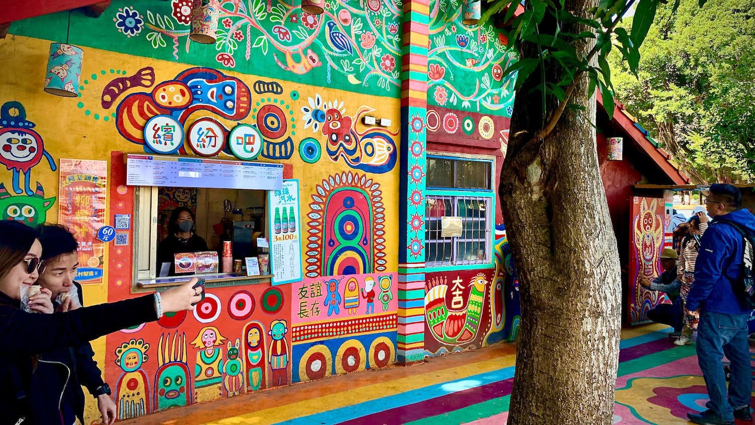 People taking selfies outside the Rainbow Bar, a cafe at Rainbow Village, Taiwan.