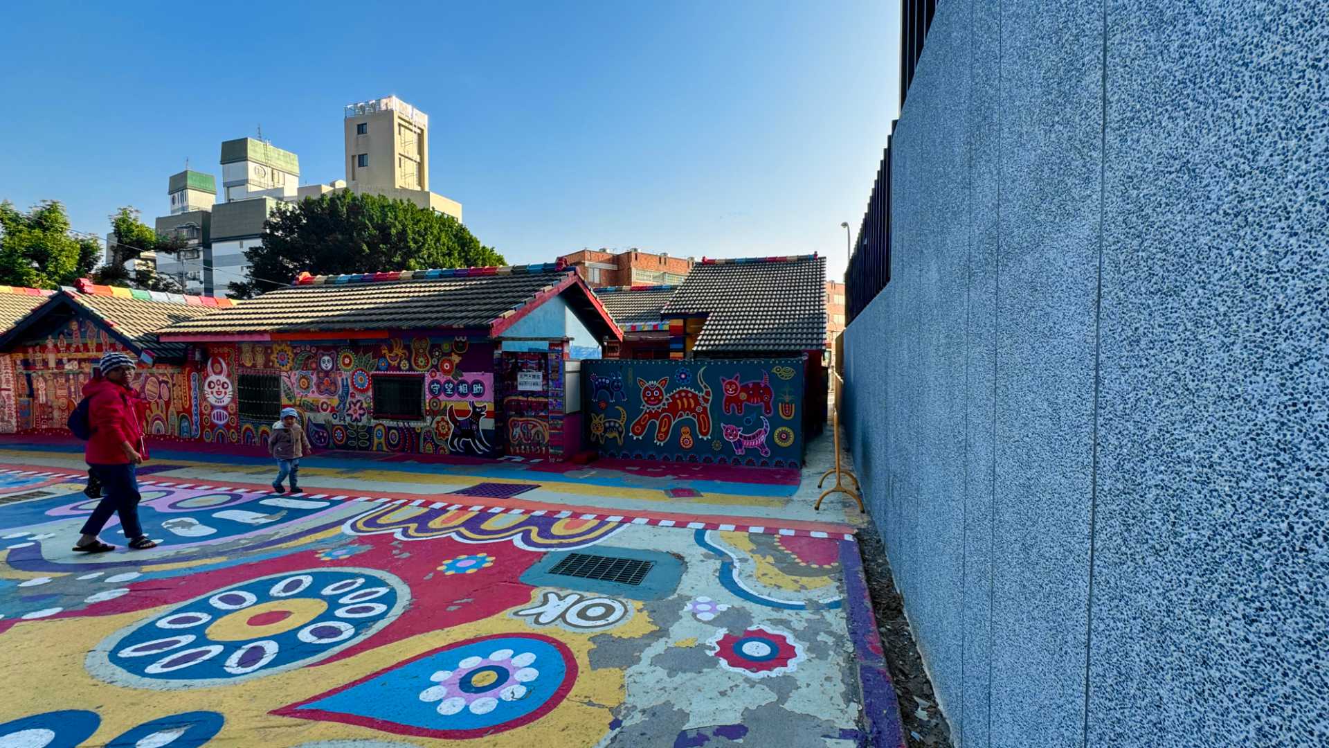 The forecourt of Rainbow Village, shaded by a new gray concrete wall on the right.