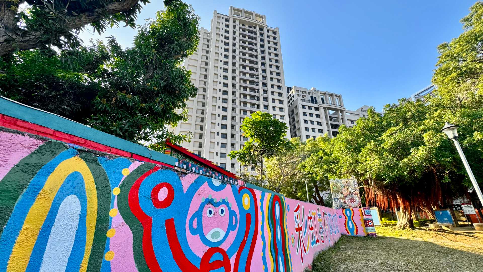 A brightly-painted wall of Rainbow Village in the foreground, and a tall apartment building in the background. The apartment building is perhaps 25 stories tall.