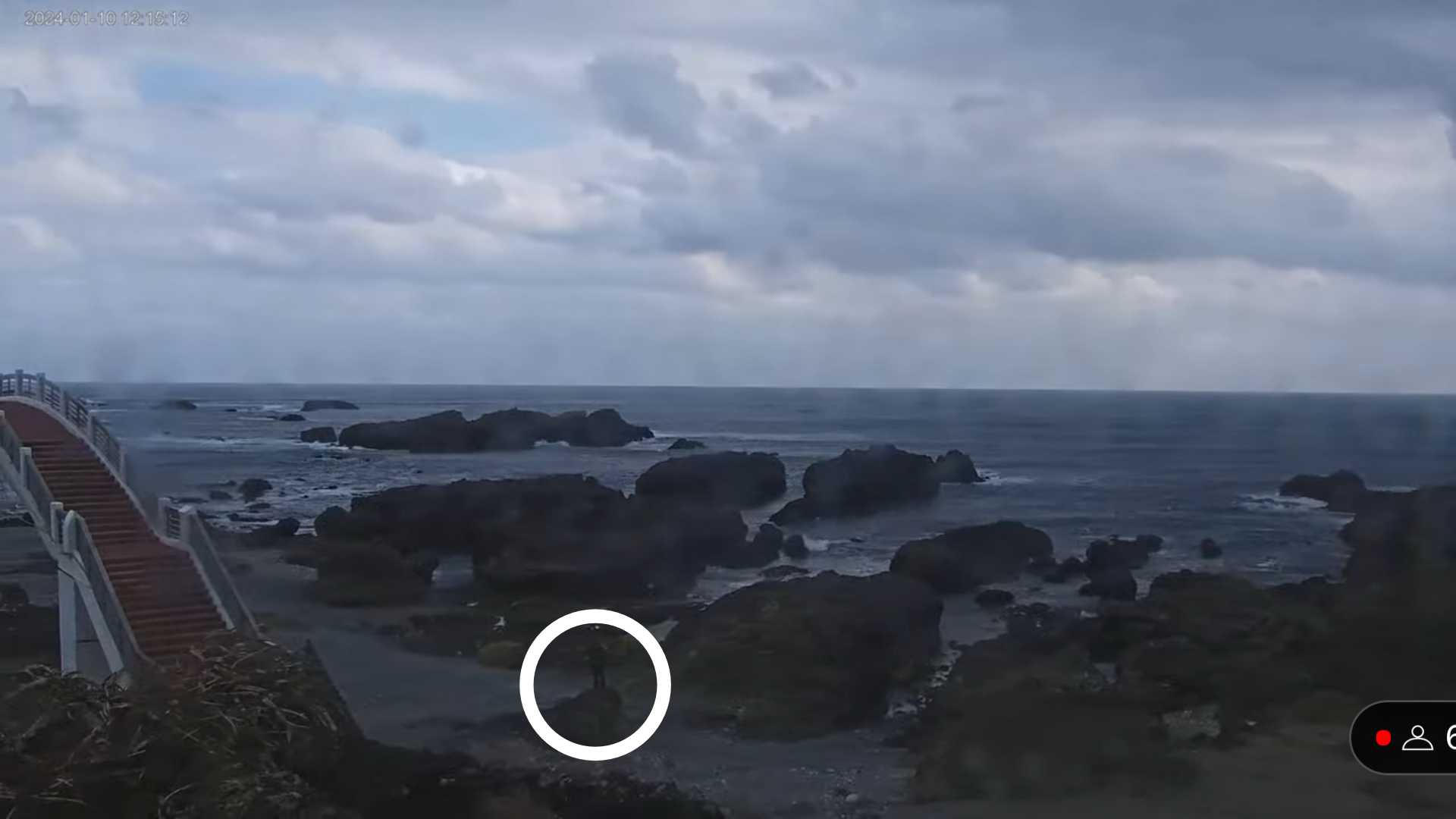Screenshot of a webcam image of a man standing on a rock next to the Sanxiantai Bridge in Taiwan. In the lower-right corner is a graphic indicating six people were watching at that moment.