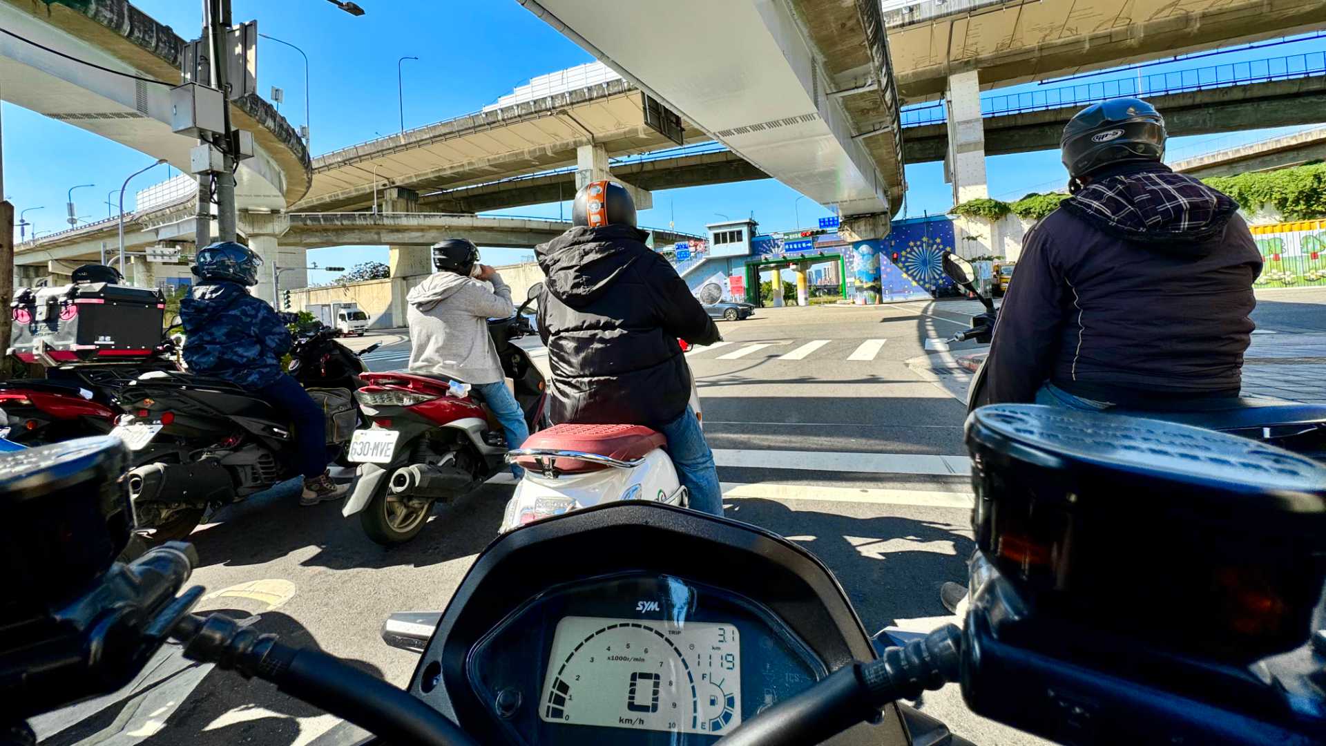 Photo taken from the point of view of a scooter rider waiting at traffic lights beneath a multi-level arrangement of overpasses in Taipei.